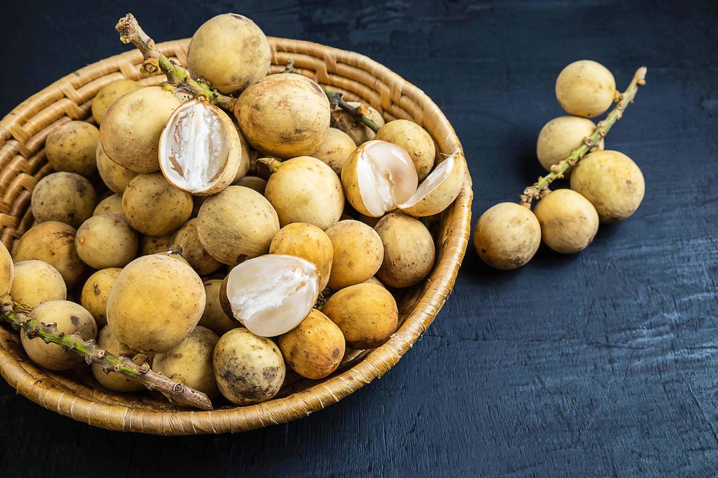 frutas longkong ou langsat em uma cesta de vime em um fundo de madeira preta foto