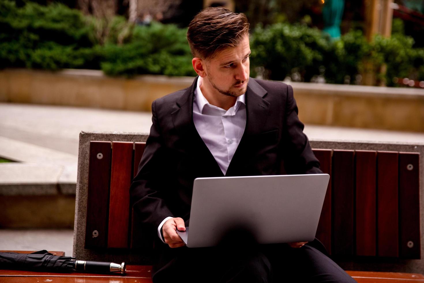 jovem cara dentro uma terno trabalho em uma computador dentro a parque do uma o negócio Centro foto