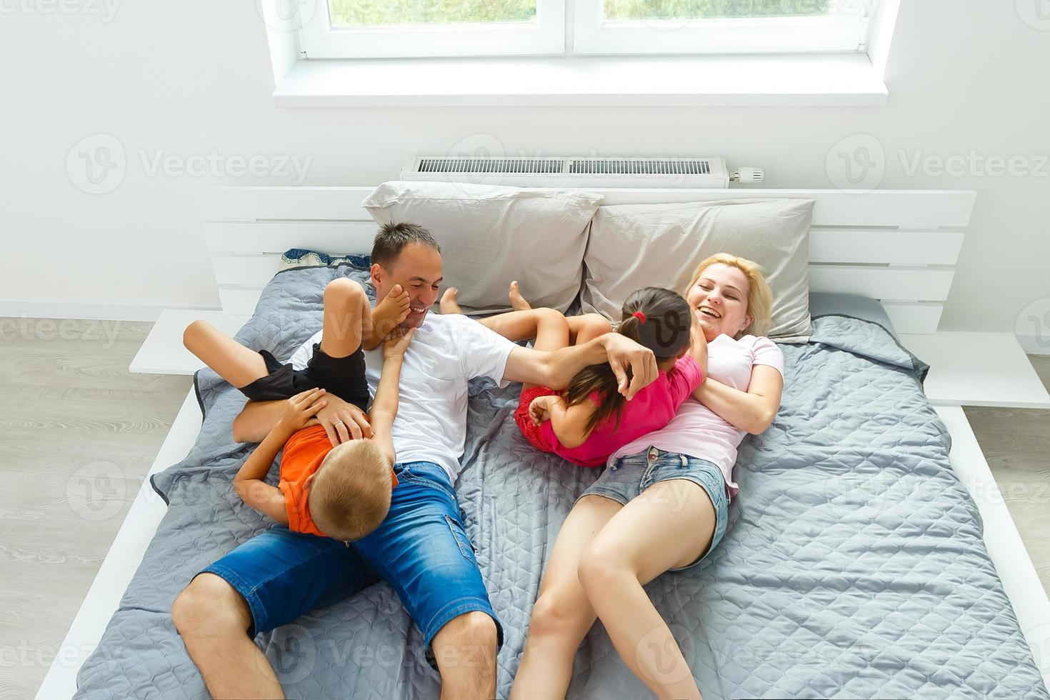 família tendo engraçado travesseiro luta em cama. pais gastos livre Tempo com seus filhas. foto