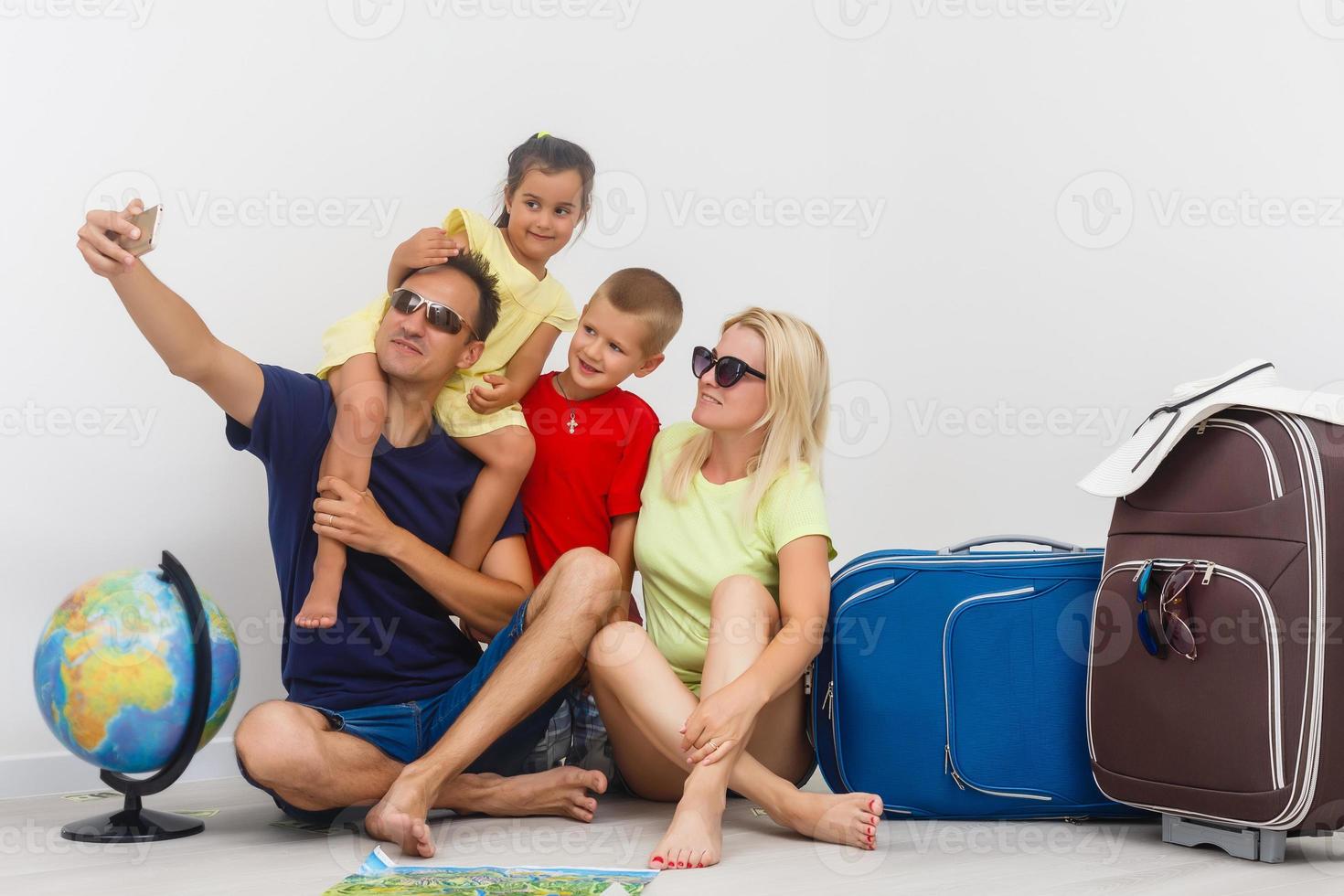 família viagem conceito - pai, mariposa, garoto, e menina sentado ao lado malas e globo, levando selfie antes jornada. isolado, branco fundo foto