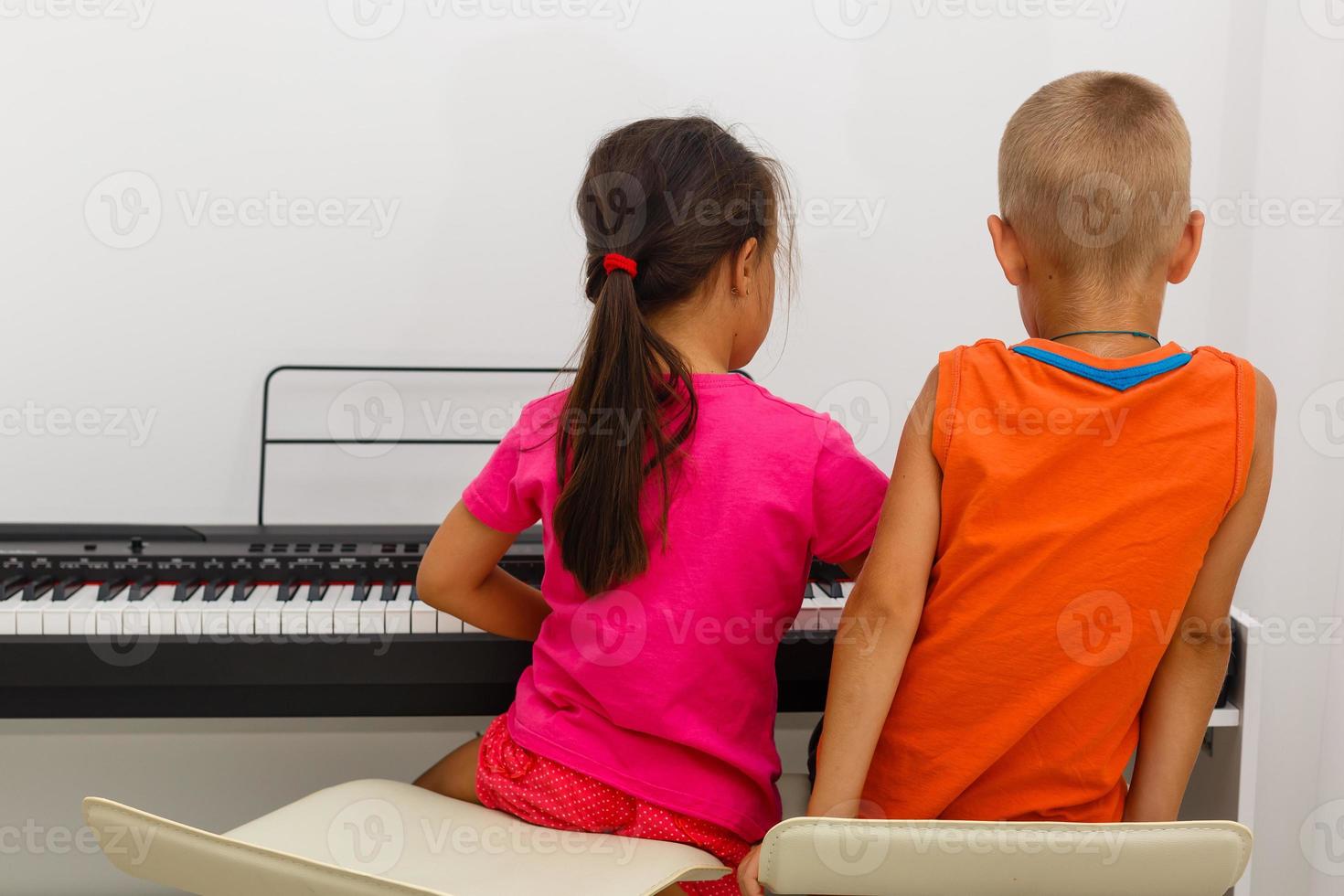 dois pequeno crianças menina e Garoto jogando piano dentro vivo quarto ou música escola. pré escola crianças tendo Diversão com Aprendendo para jogar música instrumento. Educação, Habilidades conceito. foto