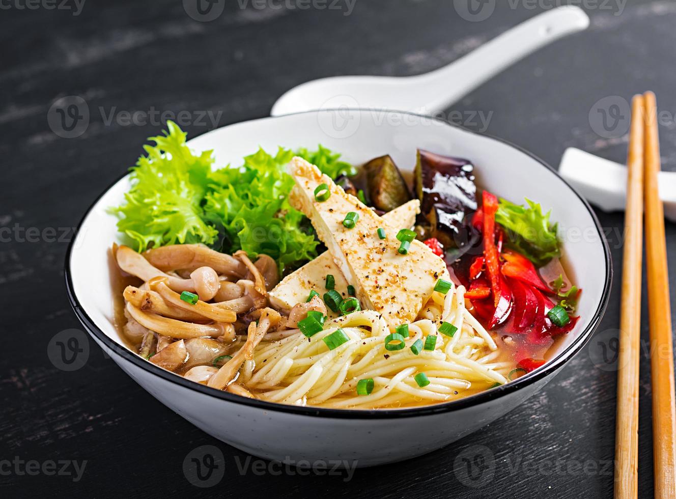 ásia vegano Macarrão sopa com tofu queijo, shimeji cogumelos e frito Berinjela dentro tigela em Sombrio fundo. foto