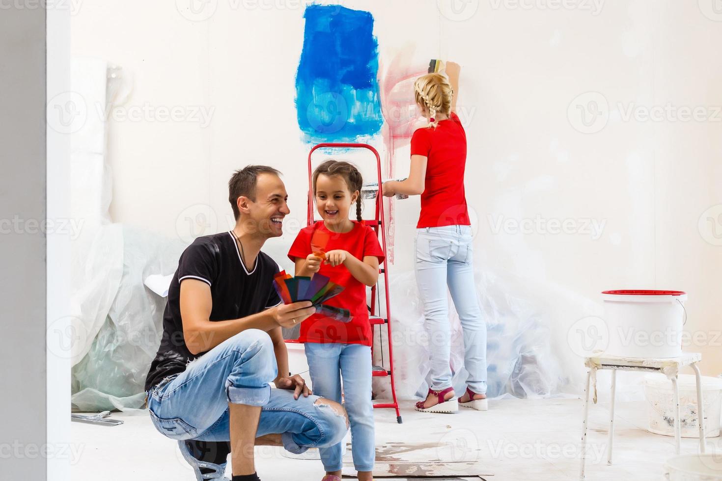 jovem família fazendo uma casa reforma e pintura quartos, a pai é pintura paredes com uma pintura rolo, a mãe e dela filho estão mexendo pintura dentro uma balde foto