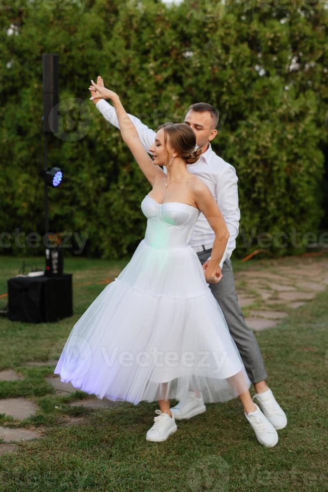 a primeiro dança do a noivo e noiva dentro uma curto Casamento vestir em uma verde Prado foto