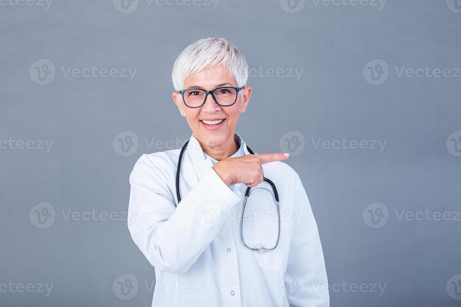 médico Senior mulher, médico profissional apontando dentro certo direção isolado sobre azul fundo. fêmea maduro médico com estetoscópio foto