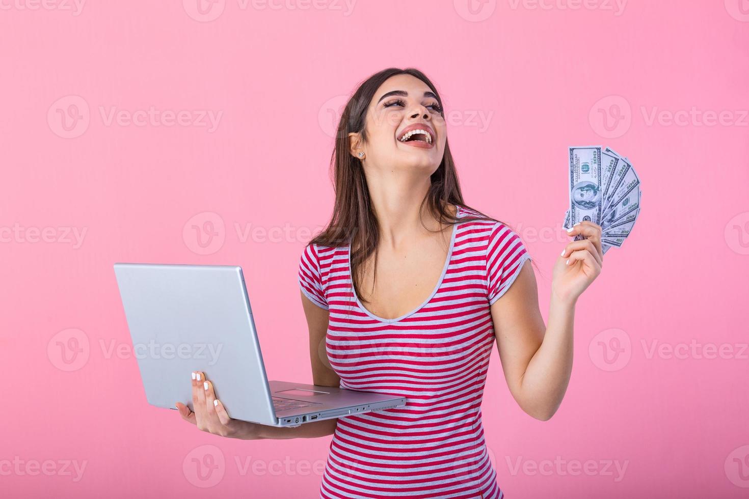 retrato do animado satisfeito menina segurando dinheiro notas com computador portátil computador isolado sobre Rosa fundo. retrato do uma alegre jovem mulher segurando dinheiro notas e computador portátil computador dentro mãos foto