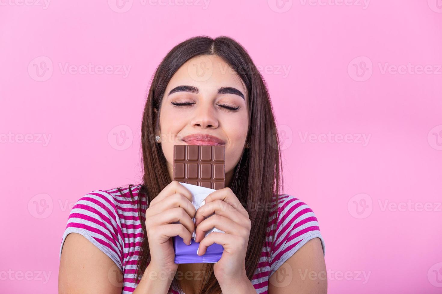 adorável sorridente Adolescência menina comendo chocolate. imagem do feliz fofa jovem mulher em pé isolado sobre Rosa fundo comendo chocolate. foto