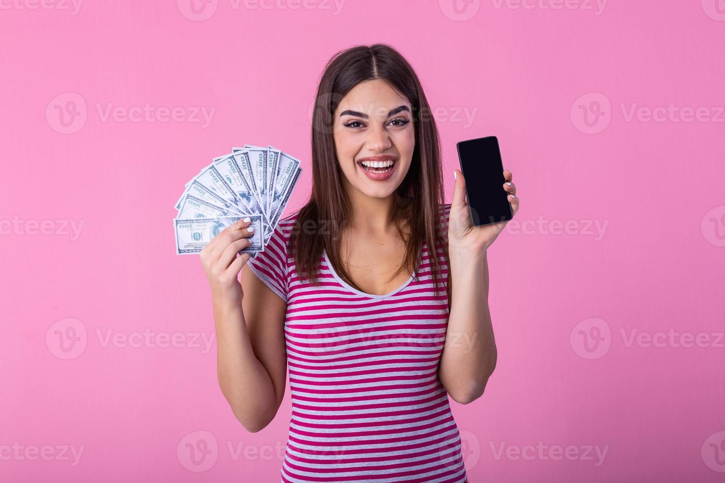 animado atraente mulher segurando Smartphone e dinheiro, dinheiro de volta. imagem do animado jovem senhora isolado sobre Rosa fundo. mostrando exibição do Móvel telefone segurando dinheiro. foto