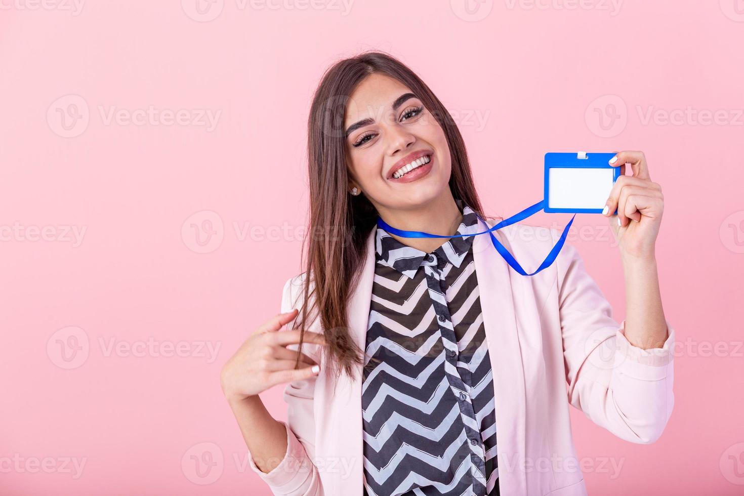 lindo sucesso mulher mostra em Câmera dela crachá e sorridente sobre Rosa muro. jovem atraente mulher segurando em branco artista cordão ou crachá dentro mão com metal pedaço. plástico passar conceito. foto