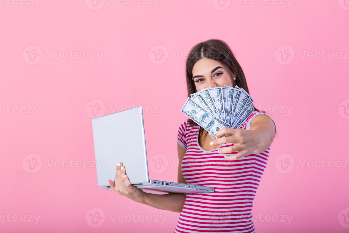 imagem do alegre jovem mulher em pé isolado sobre Rosa fundo usando computador portátil computador e segurando dinheiro notas . retrato do uma sorridente menina segurando computador portátil computador foto