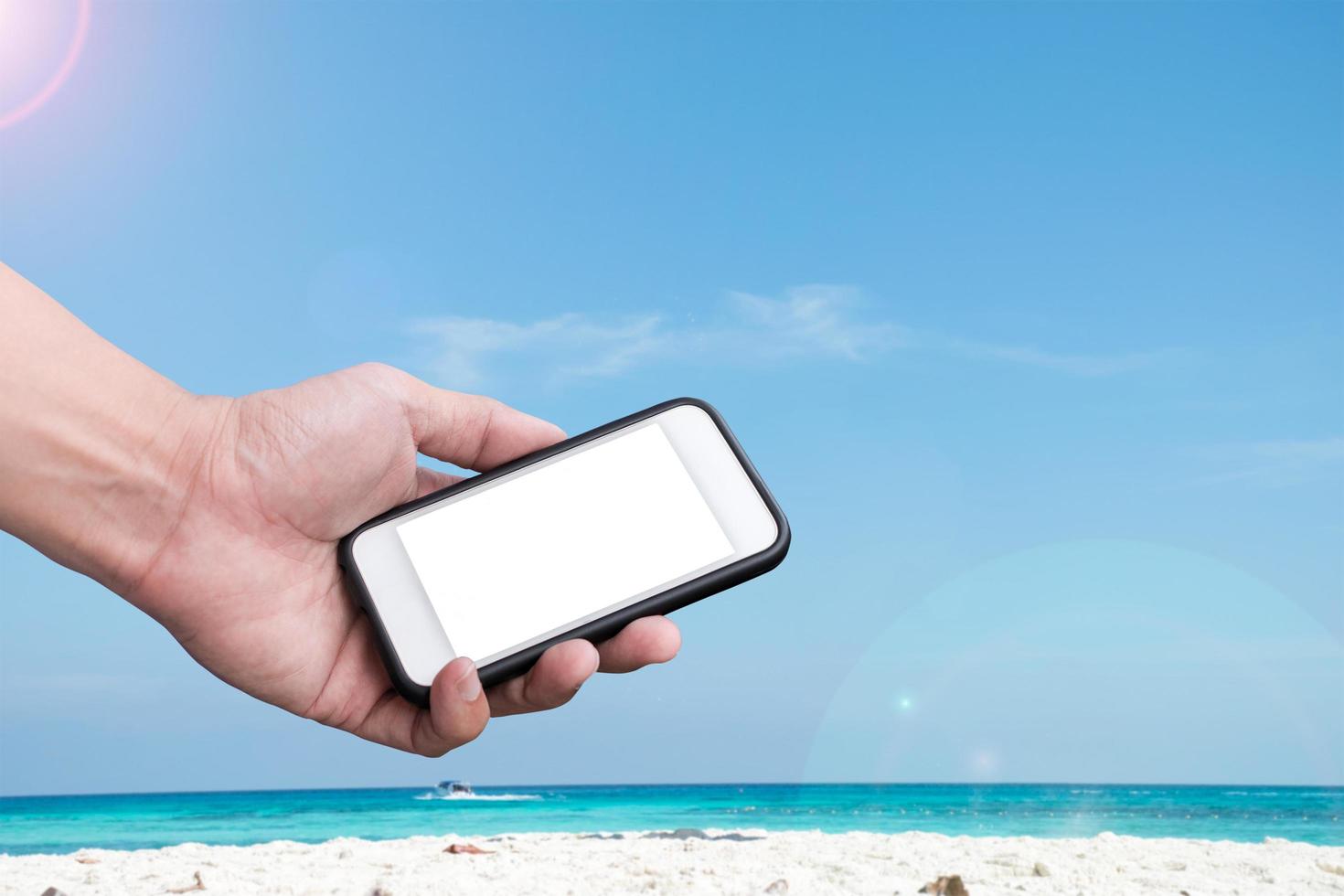 mão segurando um smartphone em uma praia e um fundo de céu azul foto