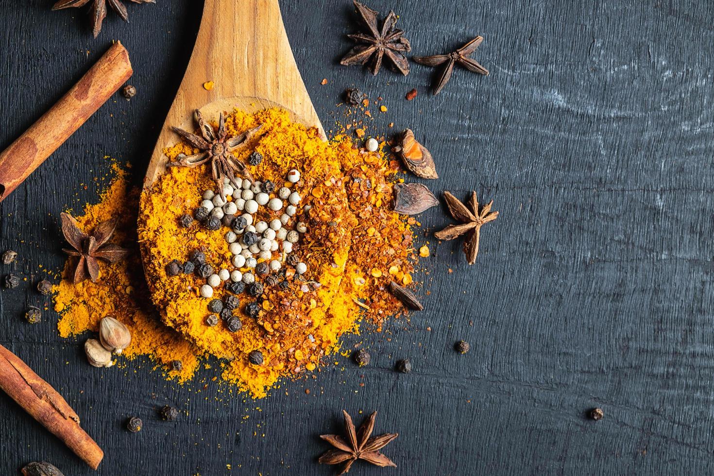 especiarias coloridas e pó em uma colher de pau sobre um fundo preto de mesa foto