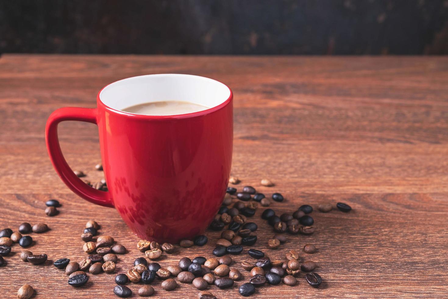 café em uma xícara de café vermelha ao lado de grãos de café derramados sobre uma mesa de madeira foto