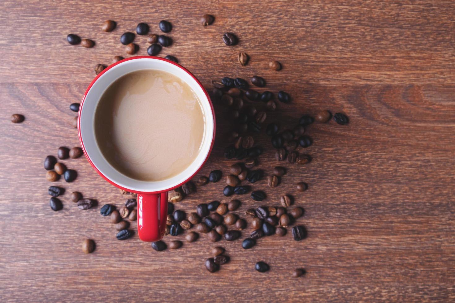 café em uma xícara de café vermelha ao lado de grãos de café derramados sobre uma mesa de madeira foto