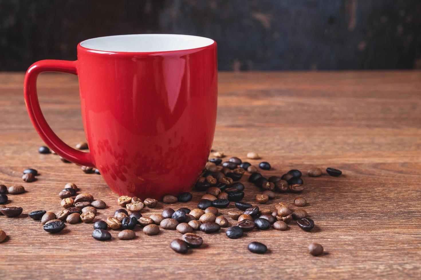 café em uma xícara de café vermelha ao lado de grãos de café derramados sobre uma mesa de madeira foto