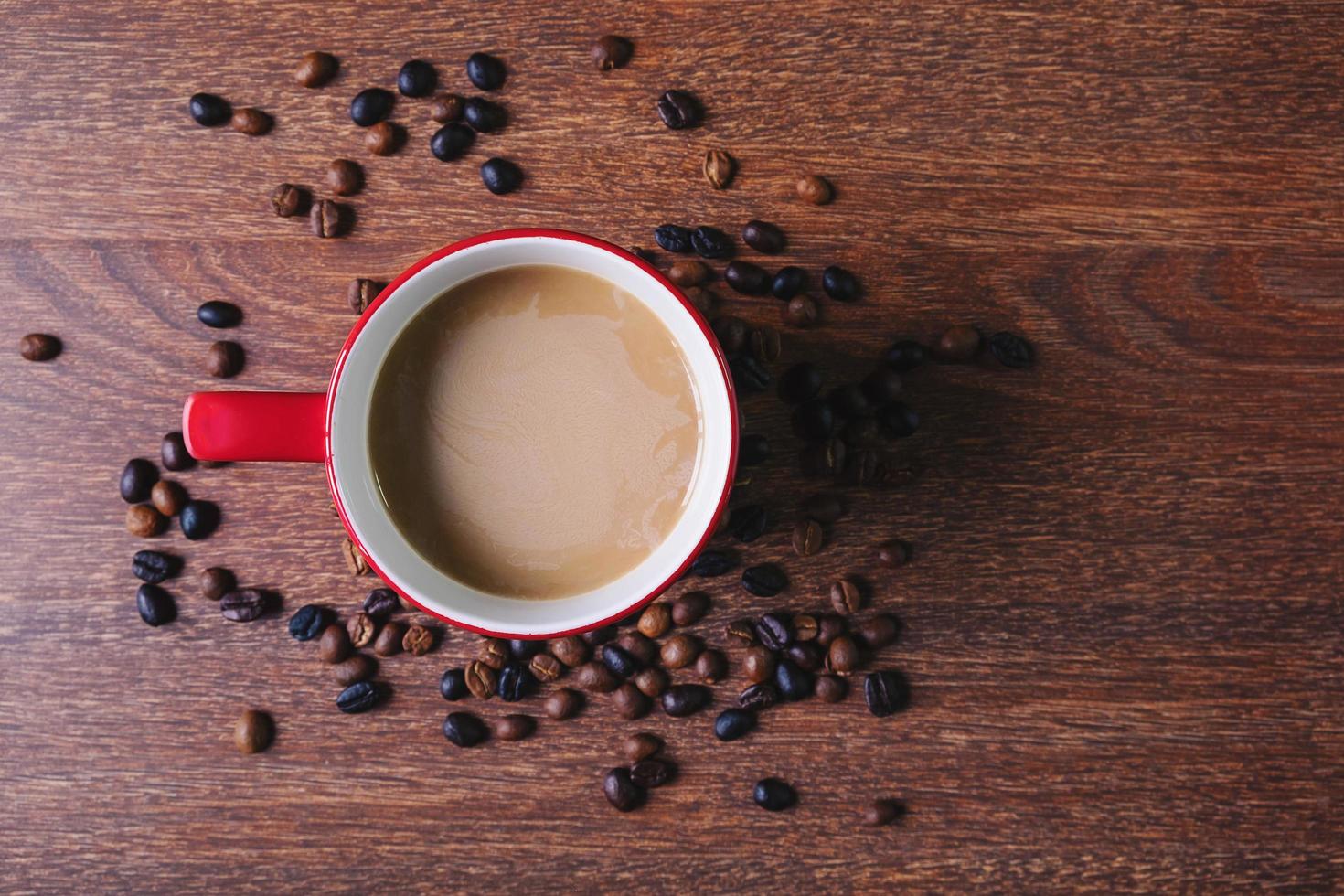 café em uma xícara de café vermelha ao lado de grãos de café derramados sobre uma mesa de madeira foto