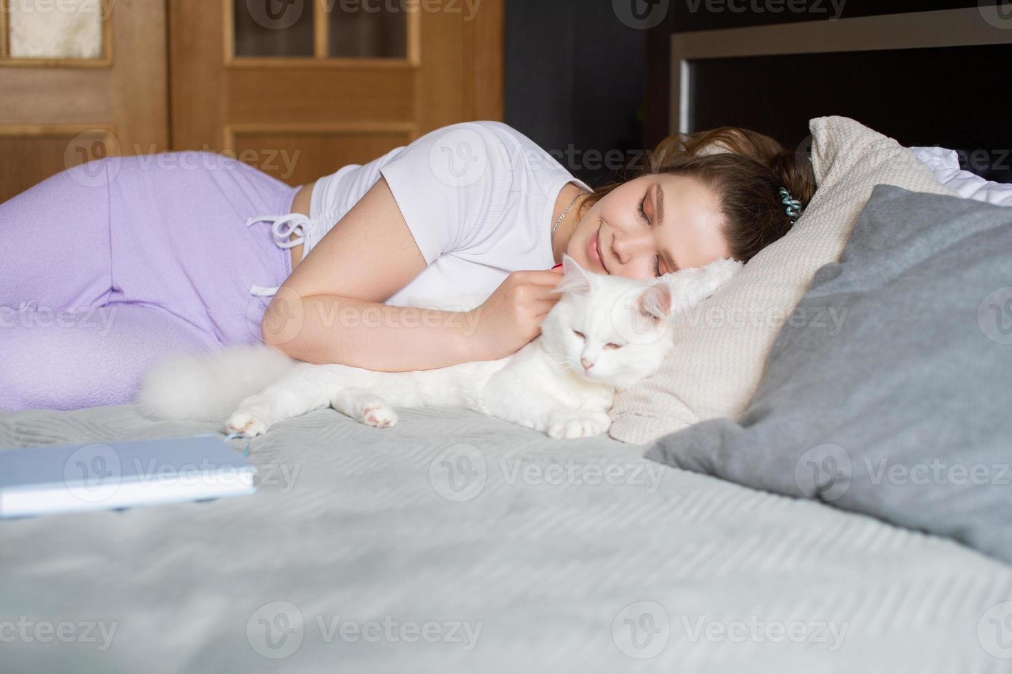 fofa menina dormindo em uma cama Próximo para uma branco gato foto