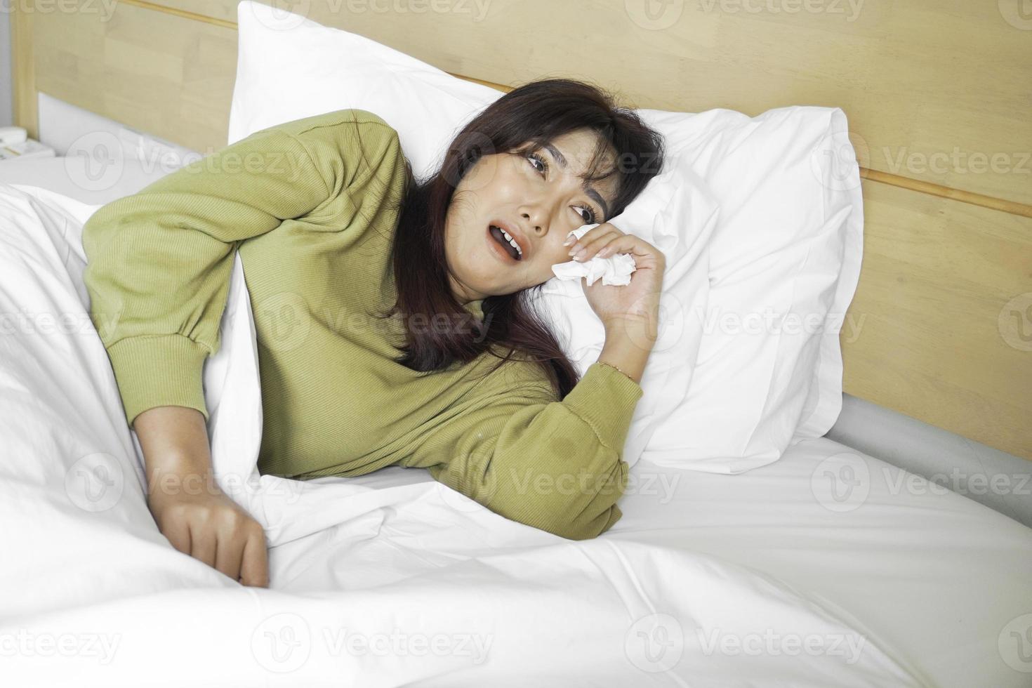 uma triste jovem ásia mulher é chorando enquanto deitado em a cama foto