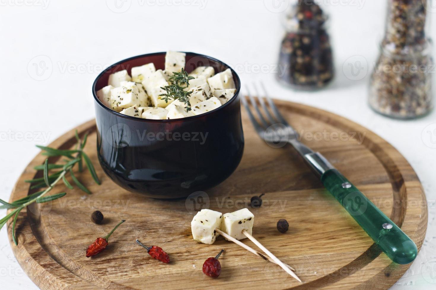 queijo feta marinado em um prato sobre uma placa de madeira com especiarias em um fundo branco foto