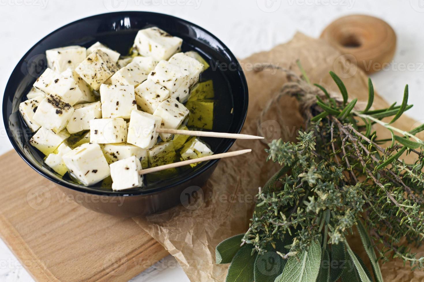 queijo feta marinado em um prato sobre uma placa de madeira com especiarias em um fundo branco foto