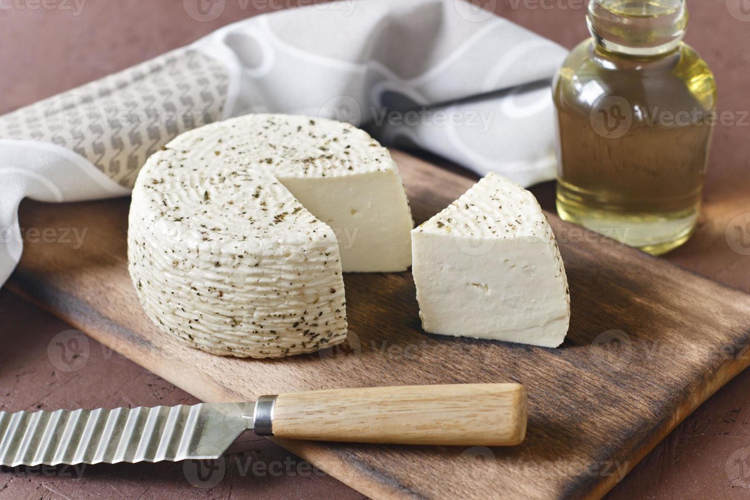 queijo branco em uma placa de madeira com azeite em um fundo marrom foto