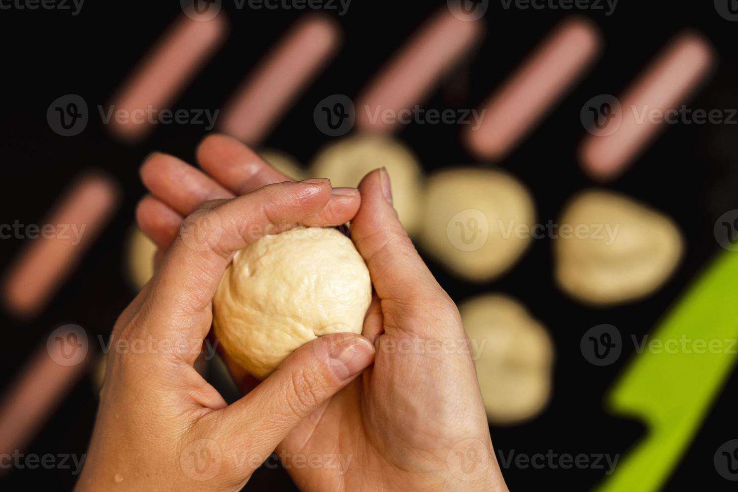 mulheres mãos esculpir uma peça do massa para cozinhando salsichas dentro massa, cozinhando quente cachorros foto