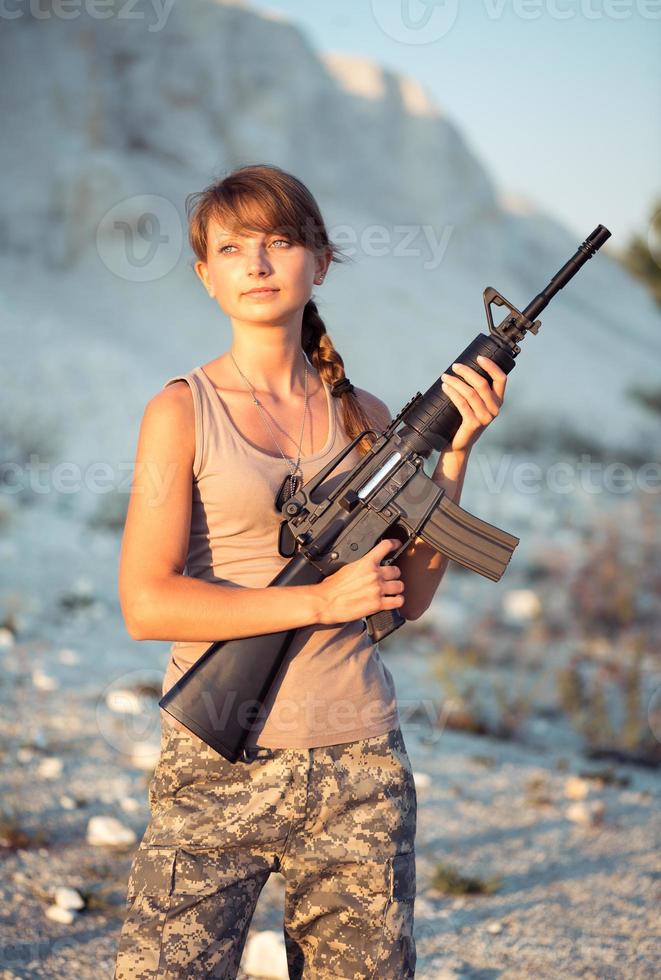 jovem fêmea soldado vestido dentro uma camuflar com uma arma de fogo dentro a ao ar livre foto