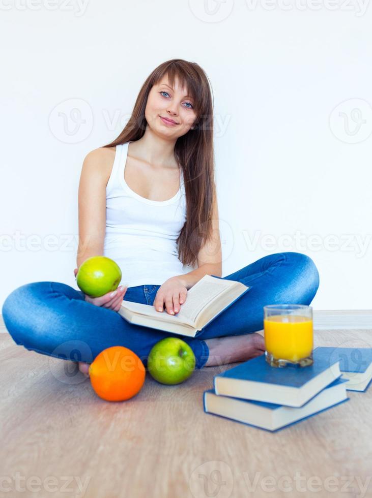 jovem morena com maçã lendo uma livro às casa foto