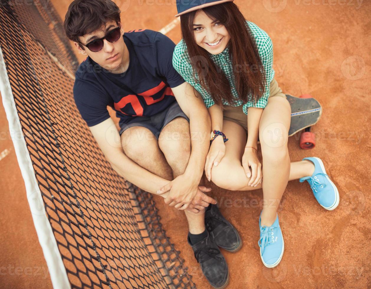 casal sentado em uma skate em a tênis quadra foto