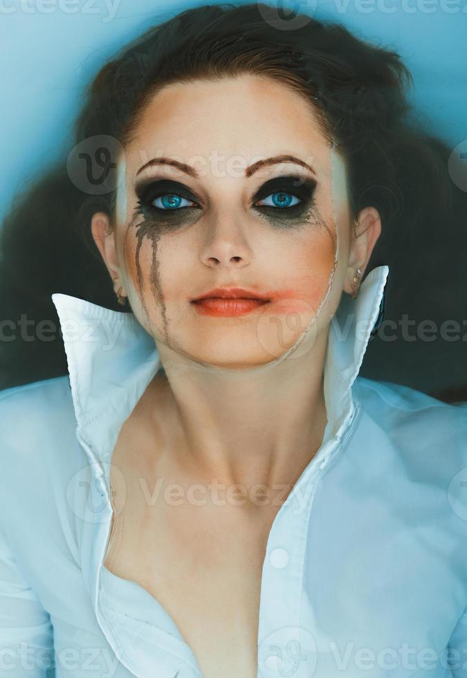 jovem atraente menina dentro uma branco camisa com manchado Maquiagem mentiras dentro a água foto