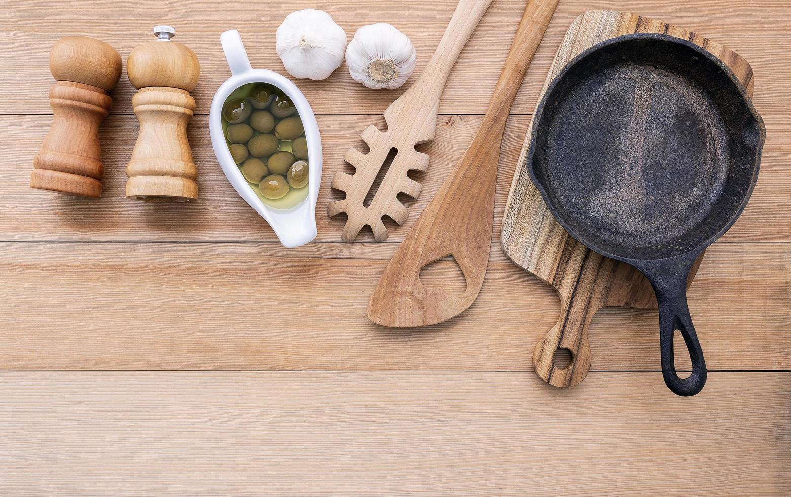 frigideira com utensílios de madeira e ingredientes frescos foto