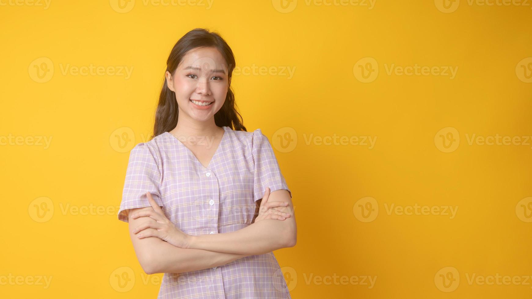 mulher asiática sorrindo com os braços cruzados e olhando para a câmera em fundo amarelo foto