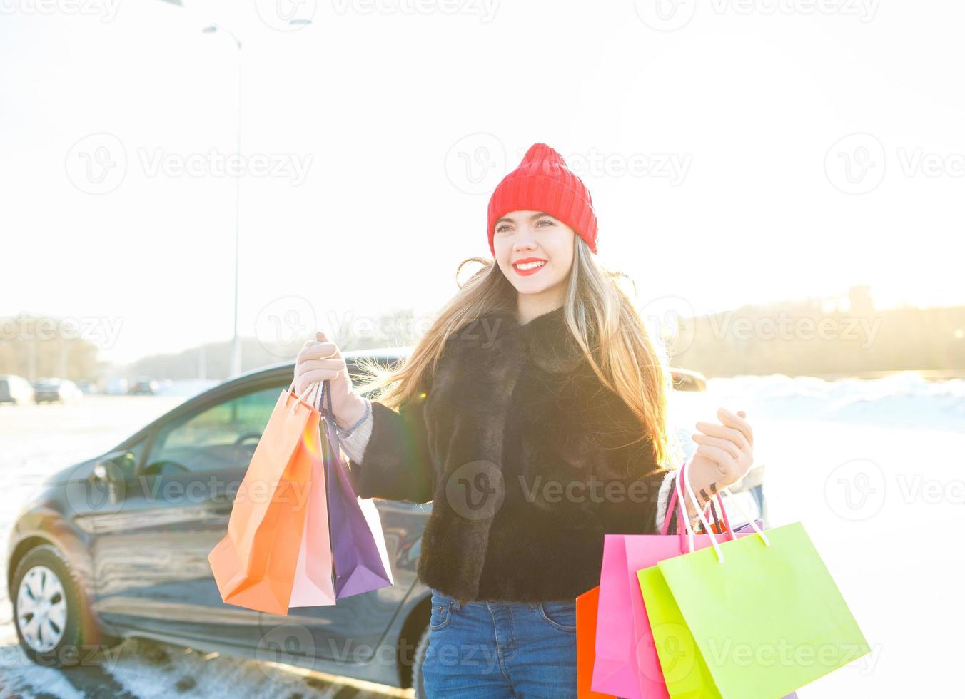 sorridente caucasiano mulher segurando dela compras saco perto a carro foto