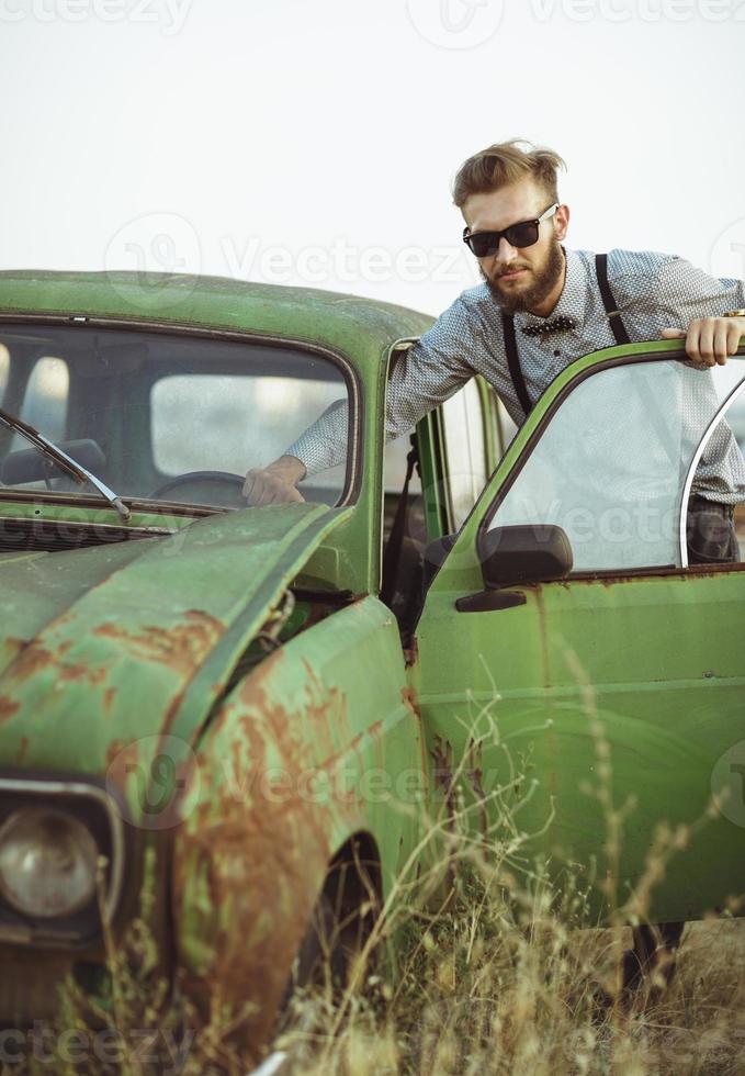 jovem bonito à moda homem, vestindo camisa e gravata-borboleta com velho carros foto