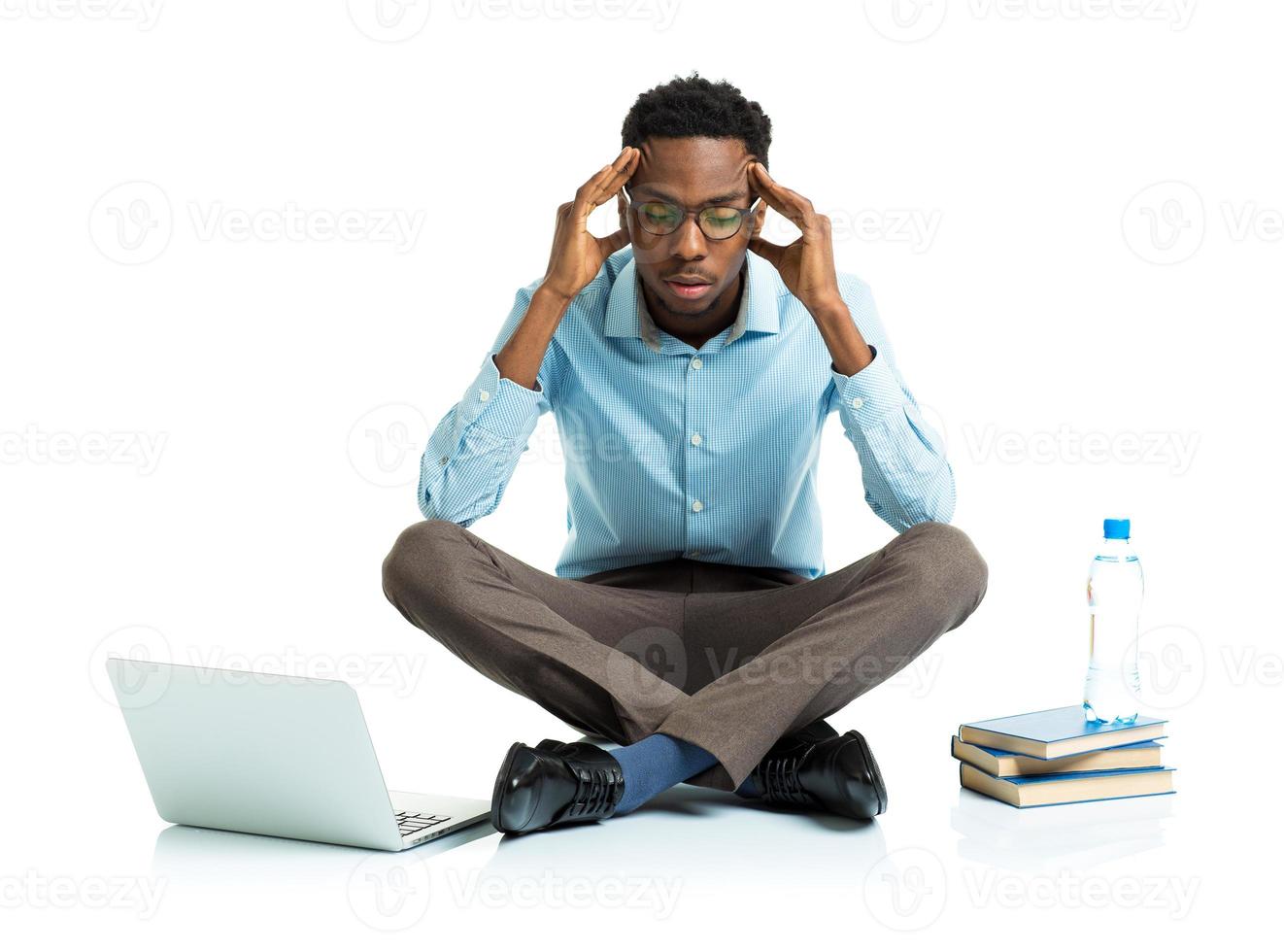 africano americano Faculdade aluna dentro estresse sentado com computador portátil, livros e garrafa do água em branco foto