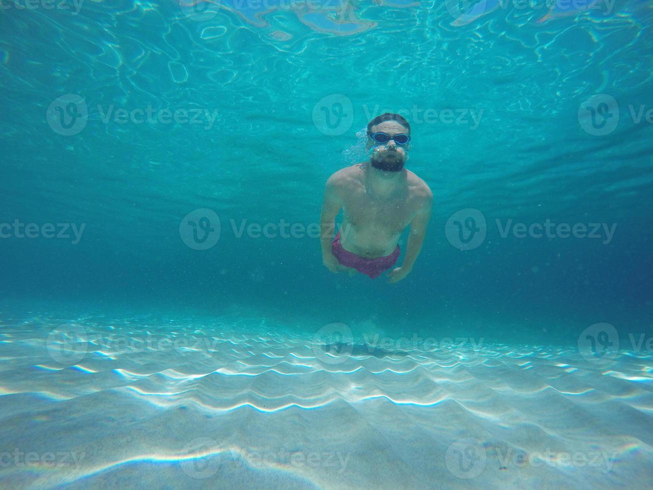 jovem barba homem com óculos mergulho dentro uma azul limpar \ limpo água foto