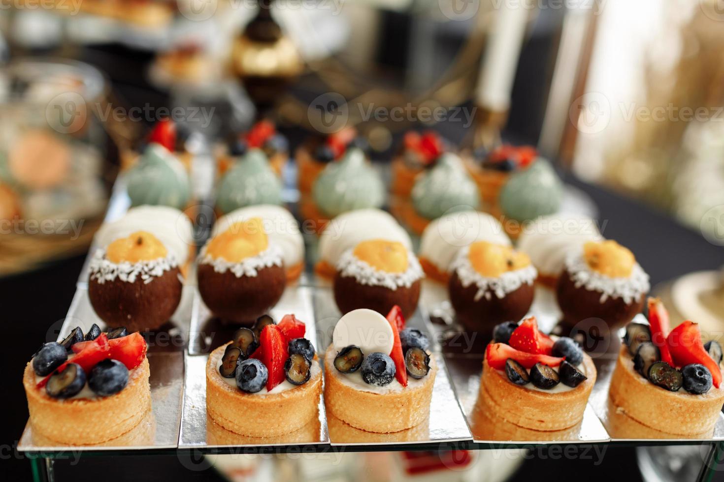 doce Barra em Casamento festa com uma muitos do diferente doces, bolos de copo, suflê e bolos em espelho placa. foto