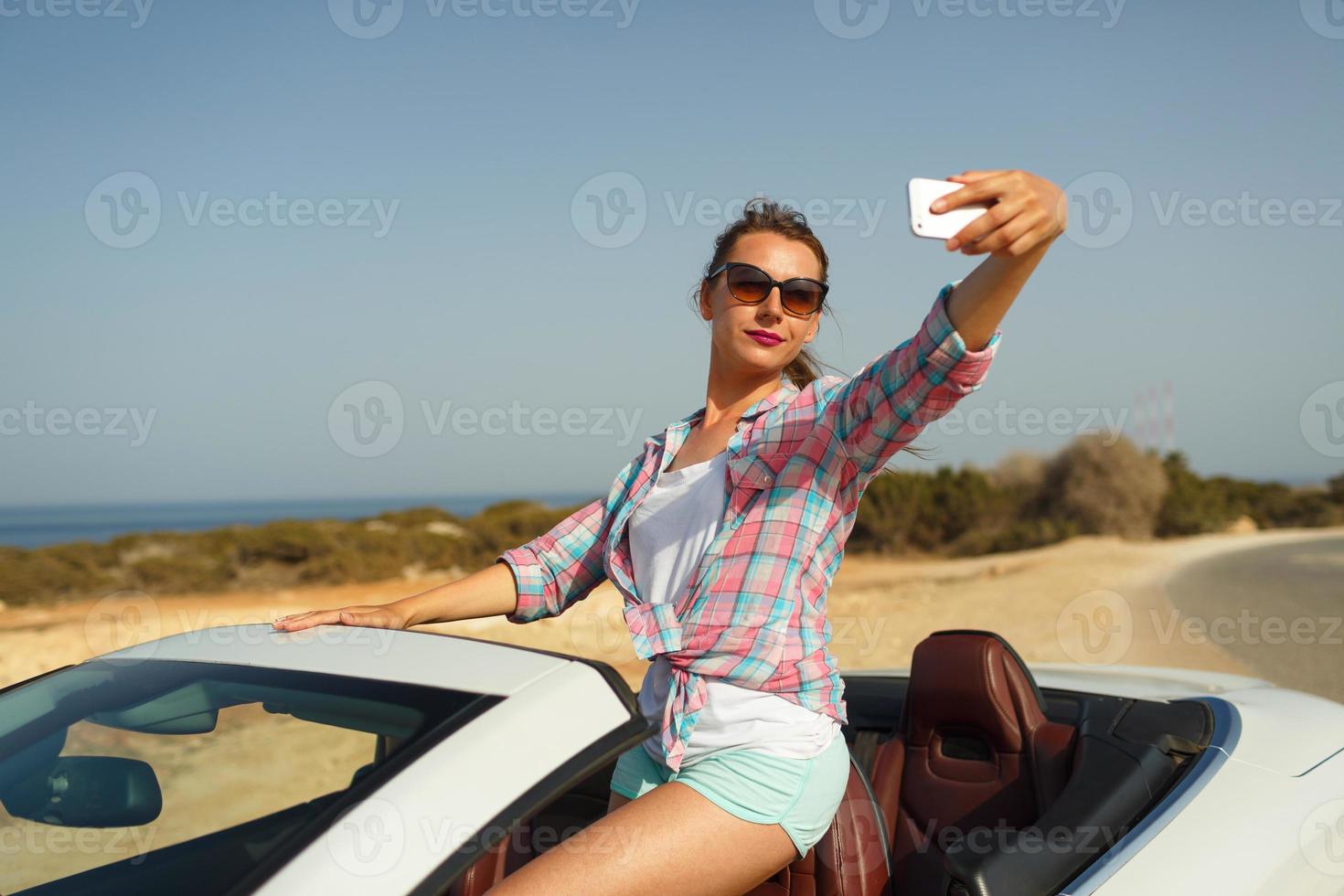jovem mulher dentro oculos de sol fazer auto retrato sentado dentro a cabriolet foto