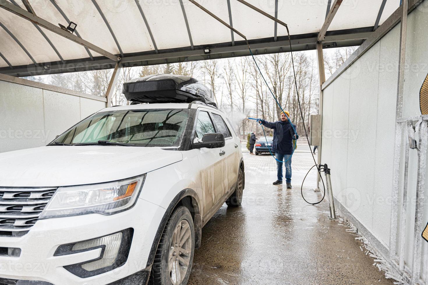 homem lavando carro suv americano com rack de teto em uma lavagem self-service em clima frio. foto