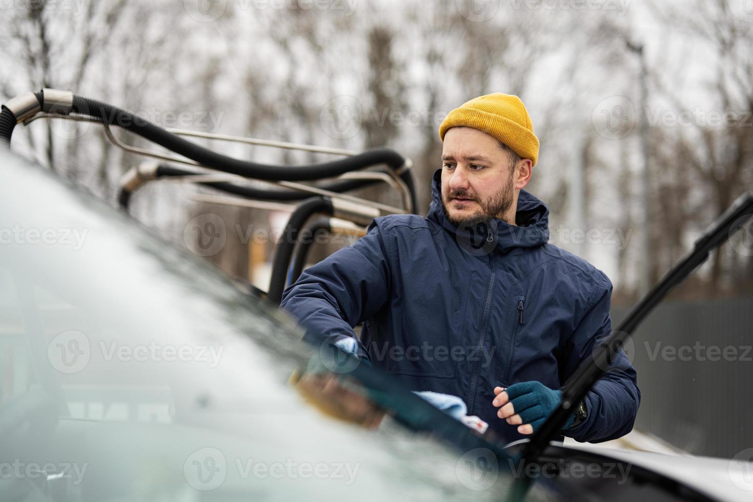 homem limpa o pára-brisa do carro suv americano com um pano de microfibra após a lavagem em clima frio. foto
