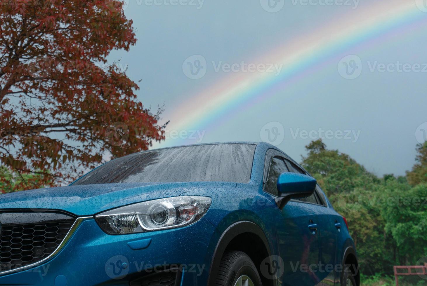 azul suv carro coberto com pingos de chuva contra verde floresta e arco Iris céu. carro estacionado às ao ar livre estacionamento muito. estrada viagem viagem. aventura viagem dentro nacional parque. segurança dirigindo dentro chuvoso estação conceito foto