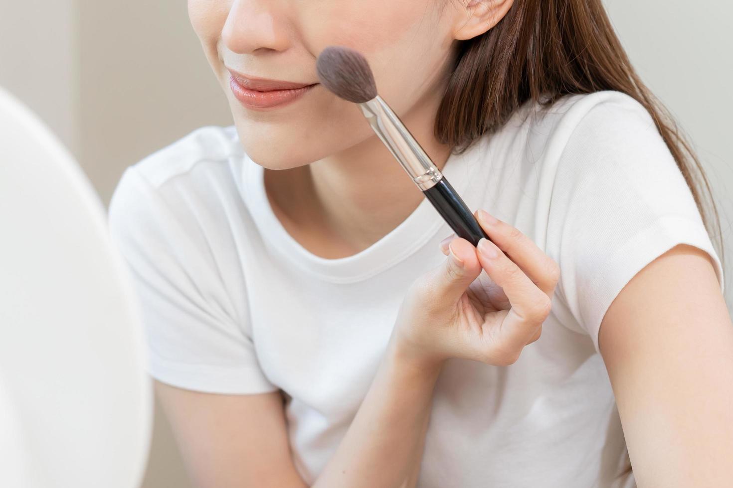 feliz rotina beleza conceito, bonita ásia jovem mulher, menina faço acima face de aplicando pó Fundação de escova por aí face, olhando às a espelho às lar. fêmea Veja com natural moda estilo. foto