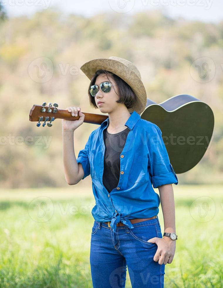 mulher usa chapéu e carrega seu violão no campo de grama foto