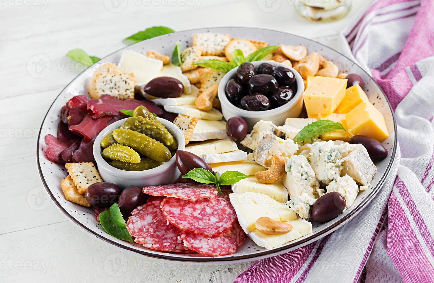 antipasto prato com basturma, salame, azul queijo, nozes, picles e azeitonas em uma branco de madeira fundo. foto