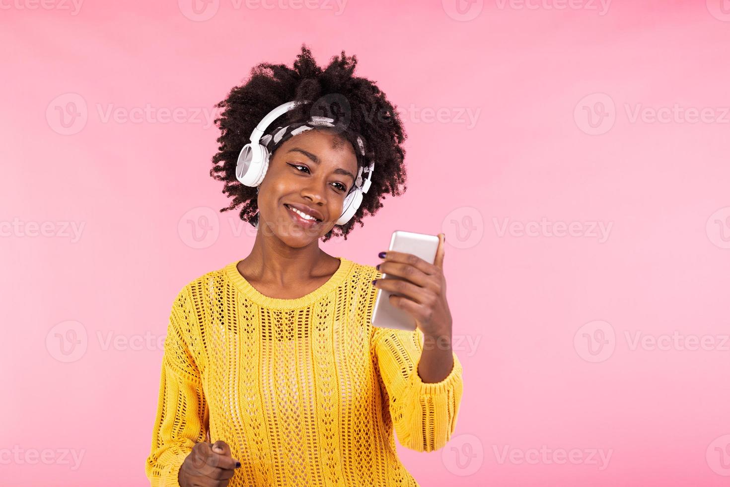 estilo de vida conceito - retrato do lindo africano americano mulher alegre ouvindo para música em Móvel telefone. na moda à moda fofa menina dentro fones de ouvido ouvindo para música dançando isolado Rosa fundo foto