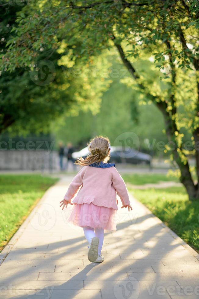 uma pequeno menina 3 anos velho dentro uma verão vestir corre longe a partir de a Câmera. a menina é virou voltar. verão tempo. foto
