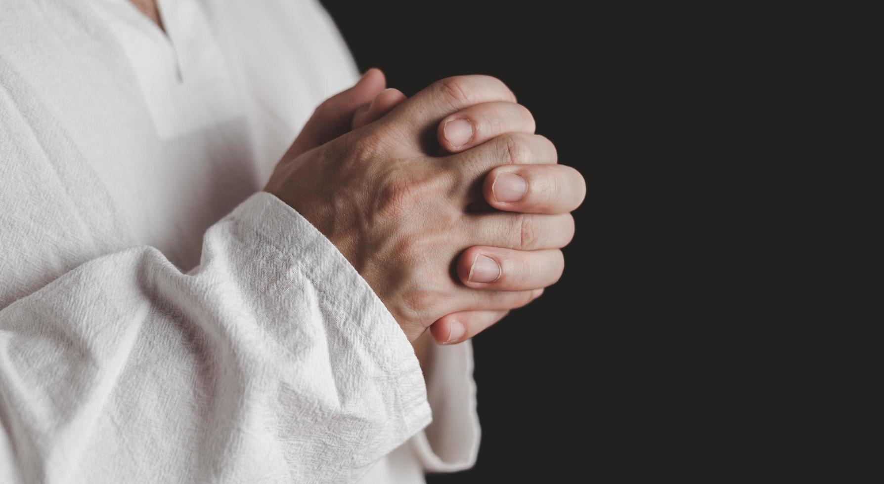 um adulto cuja mão é rezada no fundo escuro.respeito pela crença na religião e em deus. vista frontal. conceito de paz. foto