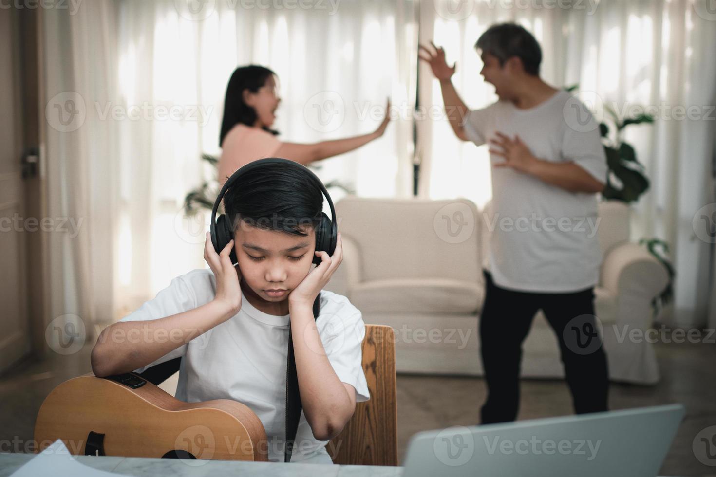 garoto asiático usando fones de ouvido e tocando música alta. para não ouvir brigas enquanto os pais brigam ou brigam em casa. problema infeliz na família, problemas domésticos na família. foto