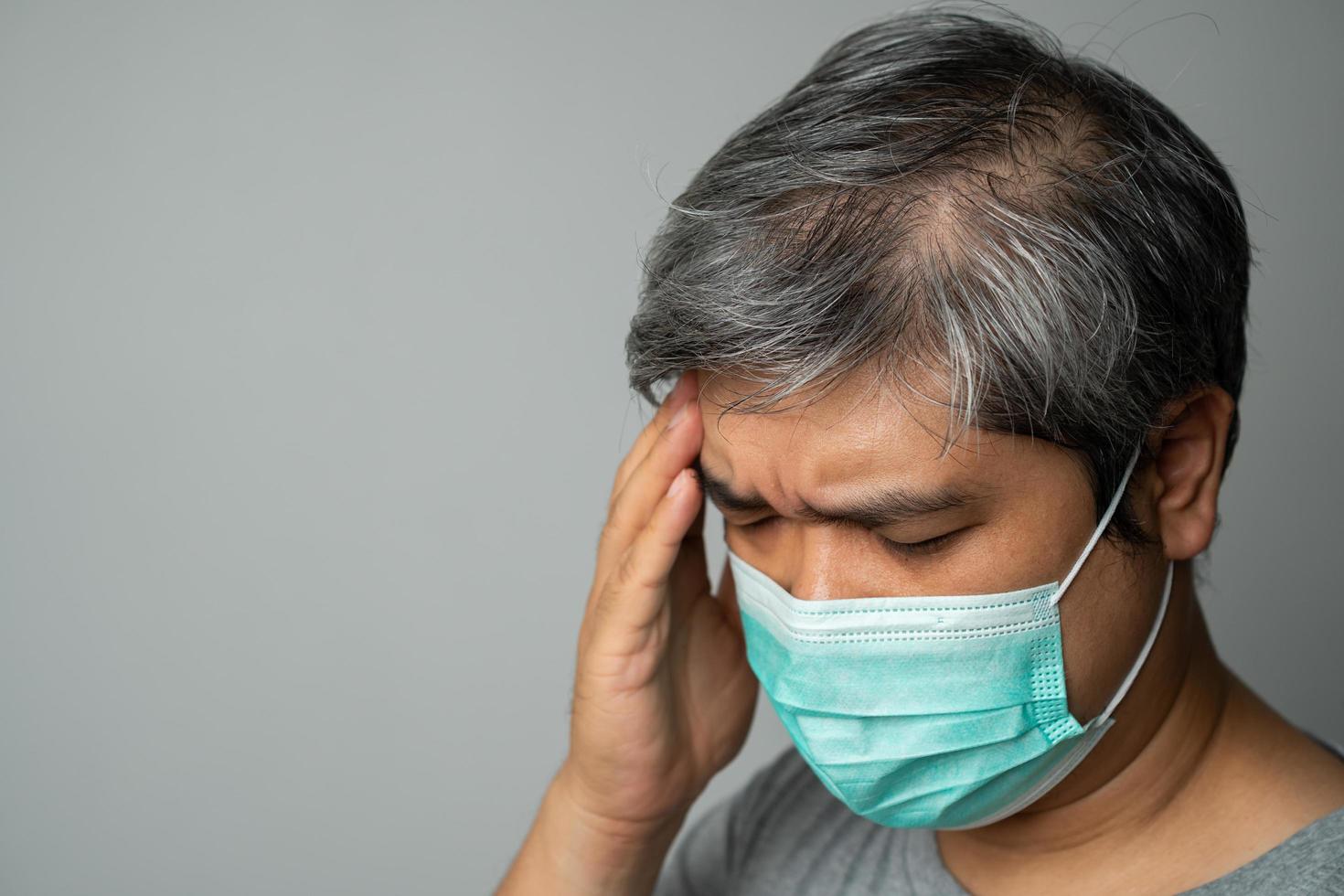 homem asiático doente usando uma máscara facial médica e pegue a mão para segurar a dor de cabeça na cabeça. conceito de proteção coronavírus pandêmico e doenças respiratórias foto