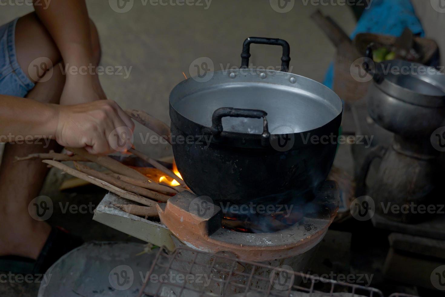 aldeões estão cozinhando Comida a partir de uma a lenha braseiro. a inferior do a Panela tem Preto fuligem enquanto culinária. a braseiro fogo é ainda usava dentro rural cozinhas dentro a norte e nordeste do tailândia. foto